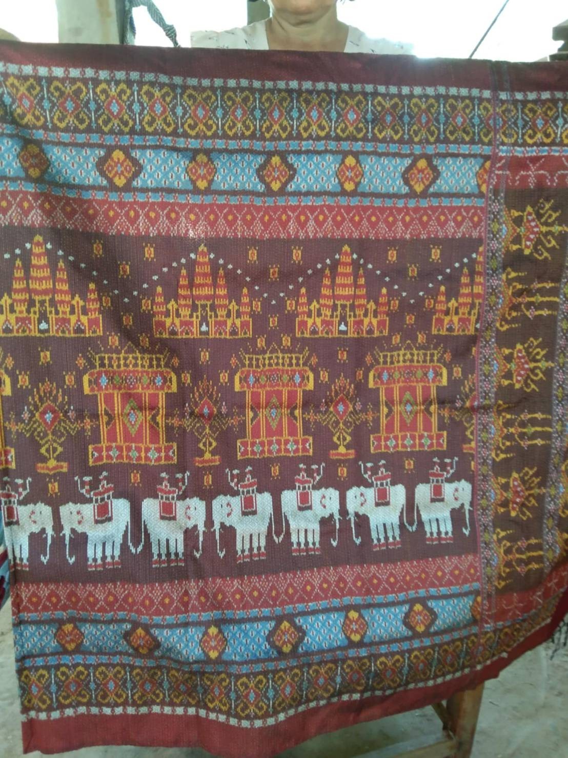 ผ้าไหมมัดหมี่ยกดอก 5ตะกอ มีหน้านาง ชายครุย ขนาด 1x2เมตร ลายช้างปราสาท สีแดงน้ำตาลเข้ม จากกี่บ้านคุณยายฐิสดา